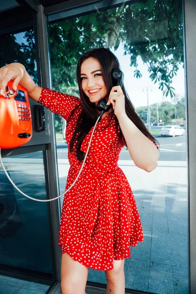 Schöne modische brünette Frau in einem roten Kleid, die am Stadthandy spricht — Stockfoto