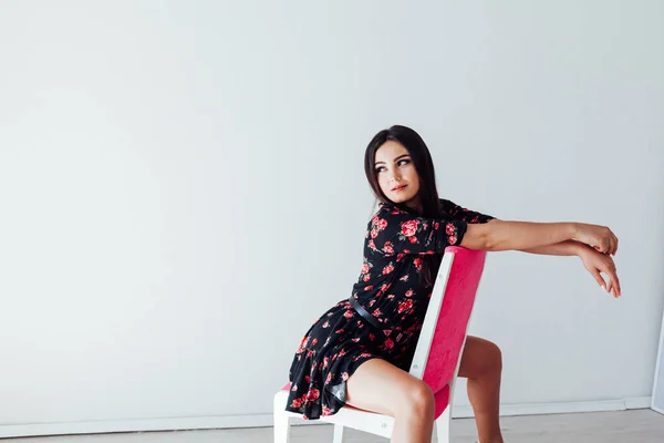Güzel, modaya uygun, çiçekli elbiseli esmer kadın pembe bir sandalyede oturuyor. — Stok fotoğraf