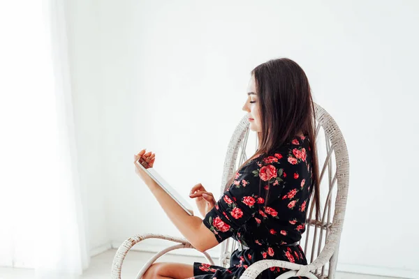 Mooie modieuze brunette vrouw in een jurk kijkt in het internet tablet — Stockfoto