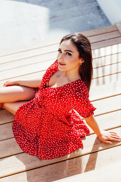 Mulher morena elegante bonita no vestido vermelho de verão senta-se nos passos — Fotografia de Stock