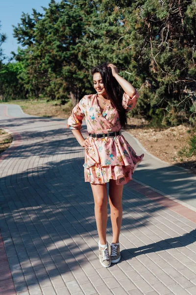Krásná módní brunetka žena v šatech s květinami procházky v parku — Stock fotografie