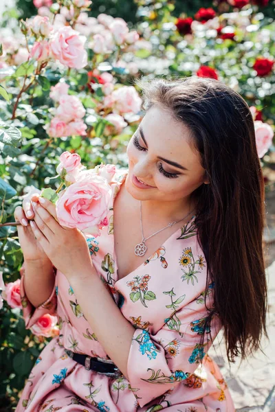 Piękne modne brunetka kobieta w sukience z kwiatami spacery zapach róż — Zdjęcie stockowe