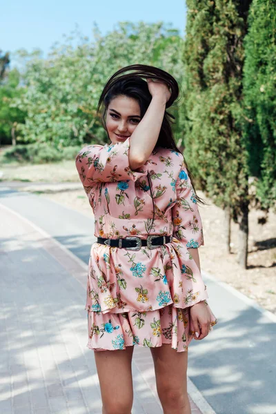 Schöne modische brünette Frau in einem Kleid mit Blumen spaziert im Park — Stockfoto