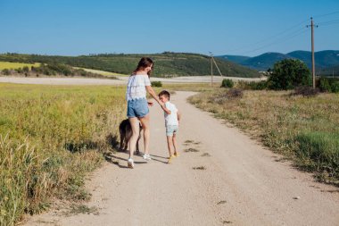 Anne ve oğlu kırsal bir yolda yürüyor.