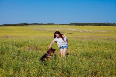 Kadın tarlada Alman çoban köpeğiyle yürüyor.