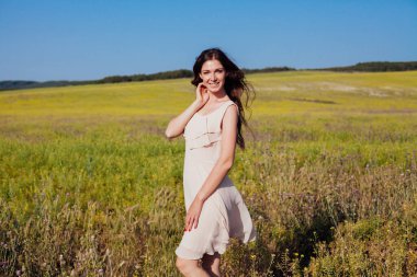 Açık renk elbiseli güzel bir kadın elinde çiçeklerle sahada yürüyor.