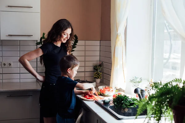 Güzel anne ve oğul salata için taze sebzeleri bıçakla kesiyorlar. — Stok fotoğraf