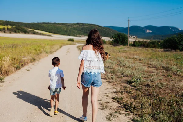 Mãe e filho caminham ao longo de uma estrada rural em um campo — Fotografia de Stock