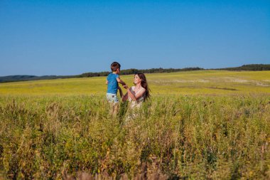 Anne ve oğlu sarı çiçeklerle dolu bir tarlada birlikte.