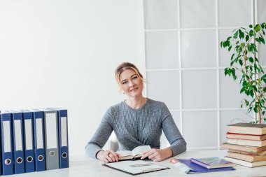 İş elbisesi giymiş güzel bir iş kadını büroda elinde belgelerle bekliyor.
