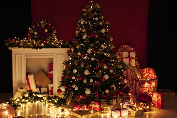 赤い背景として夜の部屋のインテリアで新年のためのガーランドライトの贈り物とクリスマスツリー — ストック写真