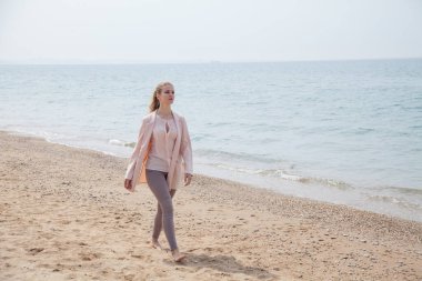 Güzel sarışın kadın deniz kenarındaki boş bir sahilde tek başına yürüyor.