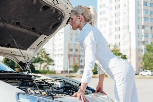 Beautiful female blonde mechanic repairs car engine — Stock Photo, Image