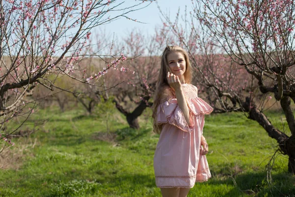 Vacker blond kvinna i rosa klänning går genom den blommande trädgården — Stockfoto