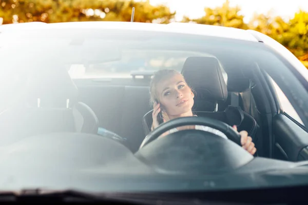 Piękna blond kierowca za kierownicą samochodu na drodze mówi przez telefon — Zdjęcie stockowe