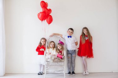 Çocuklar doğum gününde kırmızı balonlarla otururlar.