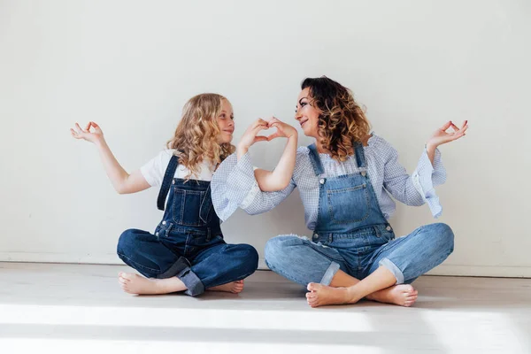 Mãe e filha de jeans estão de mãos dadas sentadas no chão — Fotografia de Stock