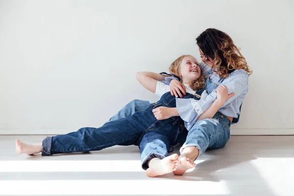 Moeder brunette en dochter blond in jeans zitten op de vloer — Stockfoto