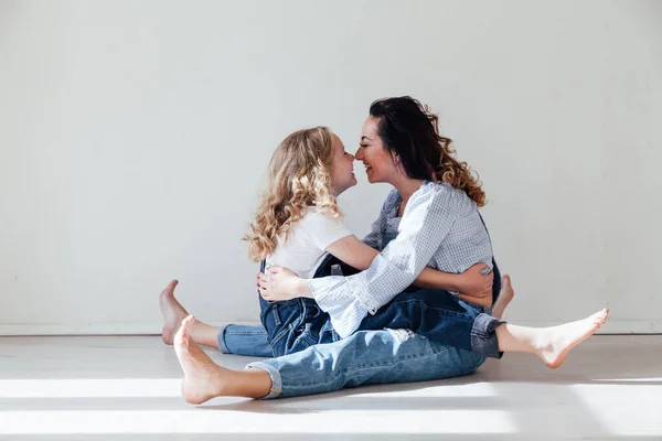 Mamma brunett och dotter blond i jeans sitter på golvet — Stockfoto