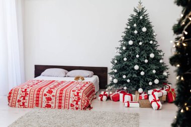 Yeni yıl kartı yatak odasının içinde kırmızı yatak dekorasyonu ve hediyeli Noel ağacı var.