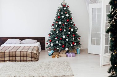 Yılbaşı arifesi yatak odasının içi kırmızı dekorlu yatak ve hediyeli Noel ağacı ile dolu.
