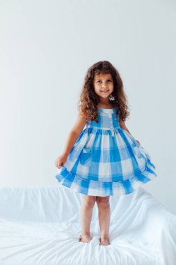 Mavi elbiseli güzel kıvırcık kız beyaz koltukta eğleniyor.