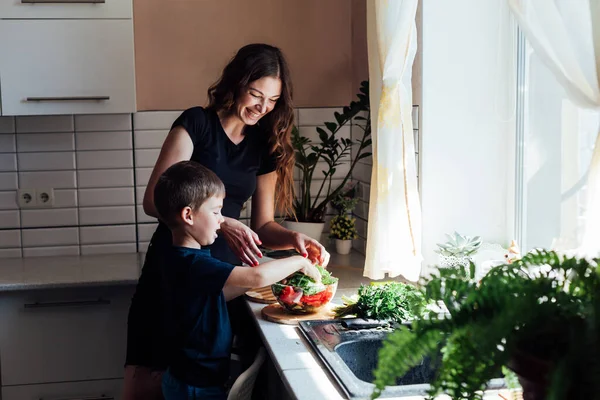 Mutter und kleiner Sohn schneiden frisches Gemüse für Salat in der Küche — Stockfoto