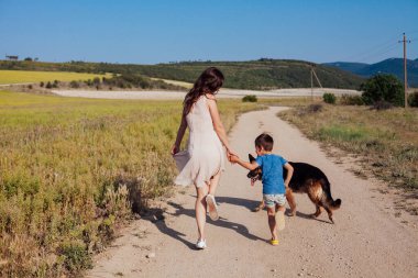 Anne ve oğlu tarlaya giderken köpekle yürür.