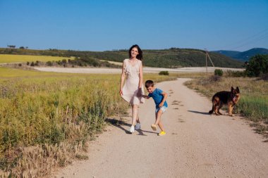 Anne ve oğlu tarlaya giderken köpekle yürür.