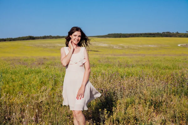 Retrato de uma bela mulher na moda em um vestido em um campo com flores amarelas — Fotografia de Stock