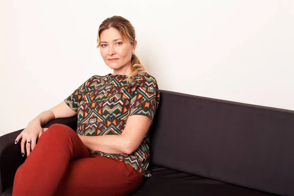 Dospělá žena ve věku 40 let sedí na černém kancelářském gauči — Stock fotografie