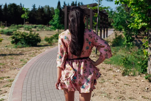 Mulher morena bonita em um vestido com flores caminha no parque sozinha — Fotografia de Stock