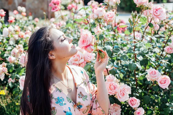 Güzel esmer kadın, çiçekli bir elbise ve güzel kokulu güller içinde. — Stok fotoğraf