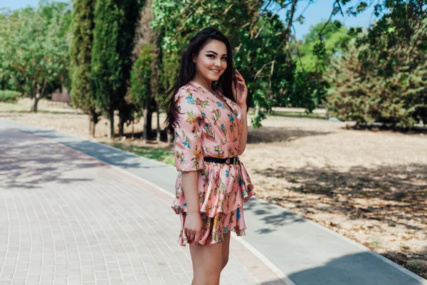 Piękna brunetka w sukience z kwiatami spaceruje samotnie po parku — Zdjęcie stockowe