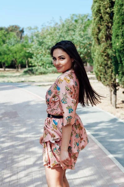 Beautiful brunette woman in a dress with flowers walks in the park alone — Stock Photo, Image