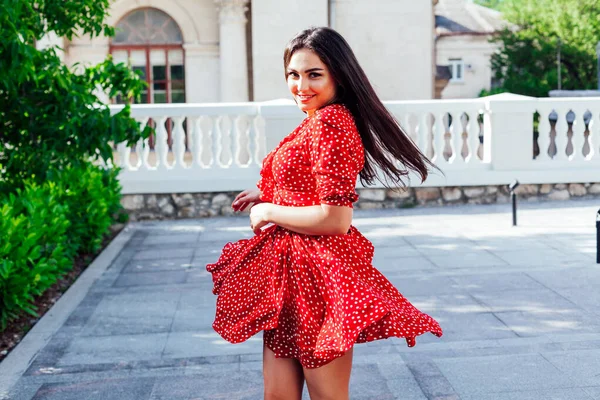 Mulher bonita morena em vestido vermelho em bolinhas caminha na rua — Fotografia de Stock