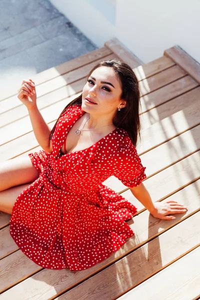 Красива брюнетка в червоній сукні в точках полоки сидить на лавці — стокове фото