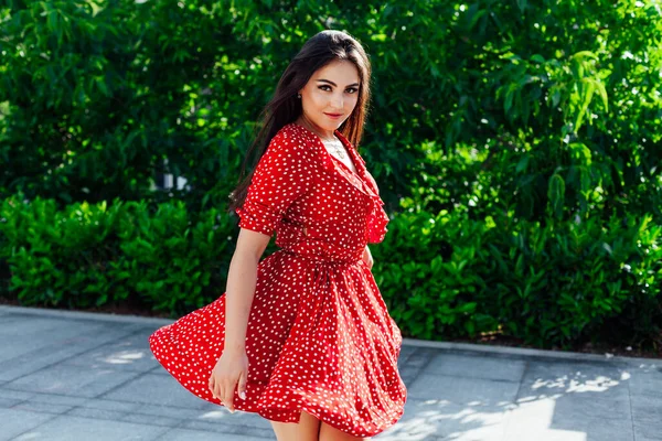 Όμορφη μελαχρινή γυναίκα με κόκκινο φόρεμα σε πουά βόλτες στο δρόμο — Φωτογραφία Αρχείου