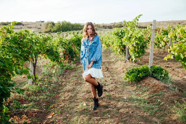 Mulher na moda bonita em jaqueta de ganga e vestido em um campo de vinhedos — Fotografia de Stock