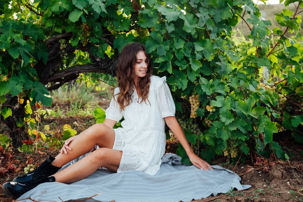 Bela mulher de vestido branco bebidas de um copo de vinho em um piquenique na vinha — Fotografia de Stock