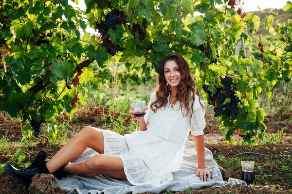 Bela mulher de vestido branco bebidas de um copo de vinho em um piquenique na vinha — Fotografia de Stock