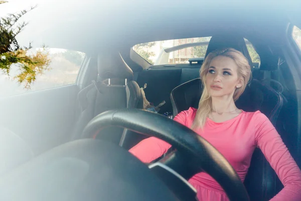 Piękna blondynka w różowej sukience za kierownicą samochodu — Zdjęcie stockowe