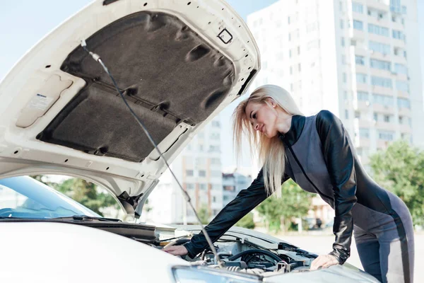Hermosa mujer rubia en la carretera repara el motor de un coche blanco — Foto de Stock