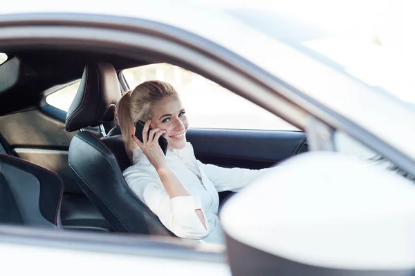 Bella donna bionda sulla strada che parla al telefono al volante di una macchina bianca — Foto Stock