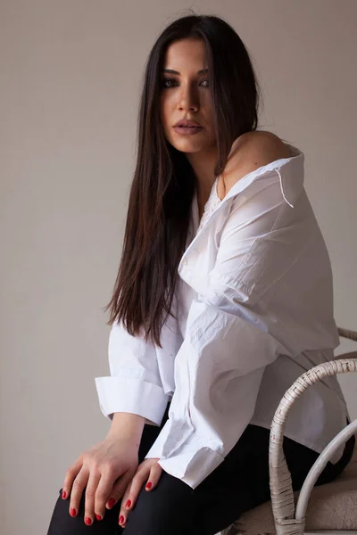 하얀 셔츠를 입은 아름다운 갈색 머리 여인이 의자에 앉아 있다 — 스톡 사진