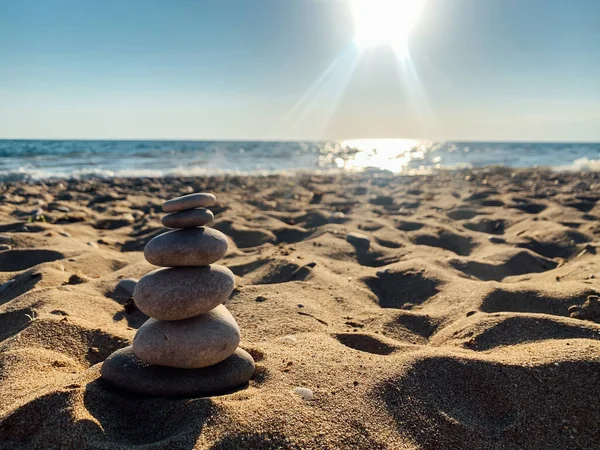 Pyramid stones balance on the sand of the beach. The object is in focus