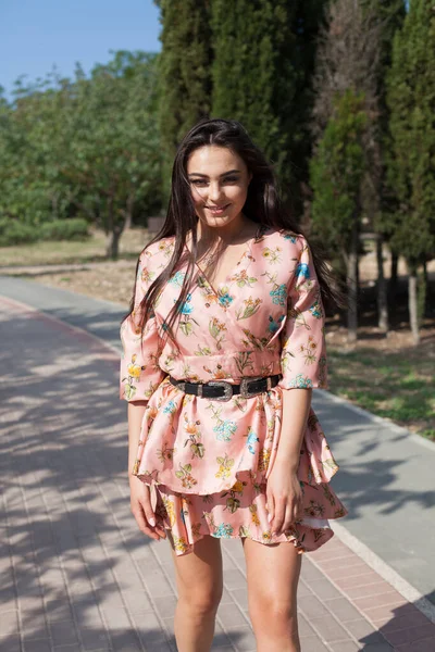 Çiçekli elbiseli güzel bir kadın parkta yalnız yürüyor. — Stok fotoğraf