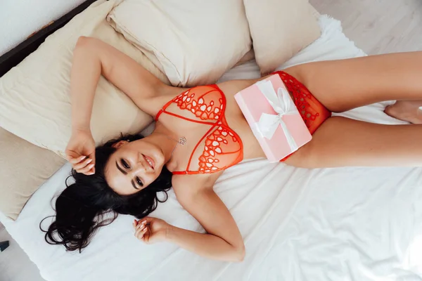 Mulher morena bonita em lingerie vermelha encontra-se no quarto na cama — Fotografia de Stock