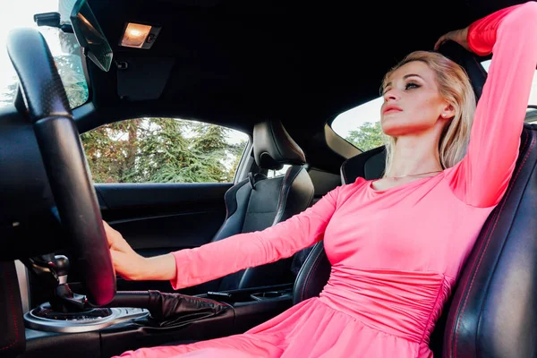 美しい女性ブロンドドライバーでピンクのドレス車の車輪の後ろ — ストック写真