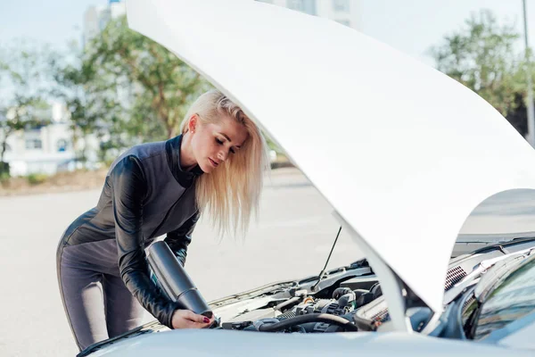 Hermosa mujer rubia conductor reparaciones motor debajo de la capucha del coche — Foto de Stock